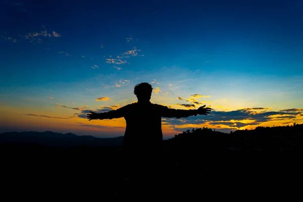 轮廓快乐的男人站在山上的日落与蓝天 享受和平时刻的概念放松或成就的概念 免版税图库图片