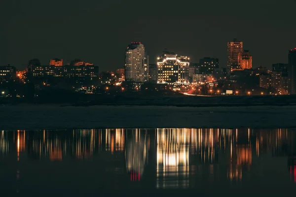 Nachtaufnahme der Stadt mit vielen Lichtern und ihrer Spiegelung in einem Flusswasser — Stockfoto