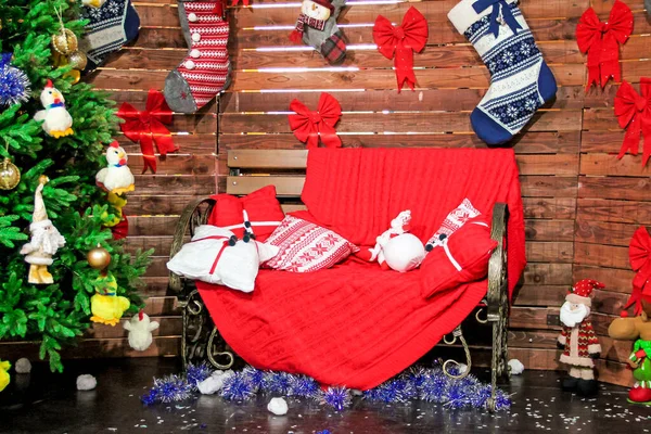 Різдвяний фон тема з різдвяними іграшками на ялинці, подушками на червоному дивані і в'язаними шкарпетками на дерев'яній стіні — стокове фото