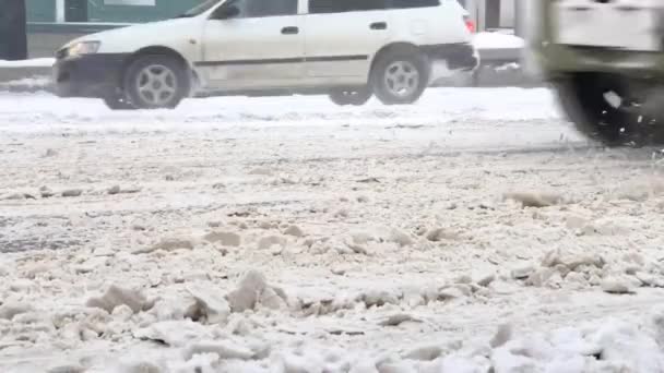 Zbliżenie jezdni pokrytej mokrym brudnym śniegiem po obfitych opadach śniegu i niższych częściach samochodów poruszających się na nim. Dangeous jazdy w warunkach śnieżnych. — Wideo stockowe