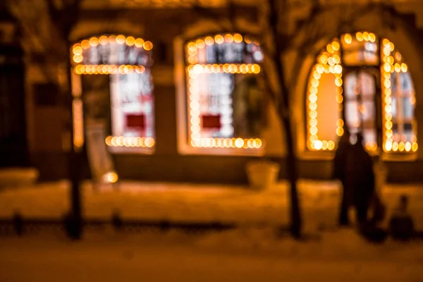 Şehir caddesinin noel ışıklarıyla çevrili pencerelerini göremiyoruz. Gece vakti. Kaldırımda yürüyen yayalar.