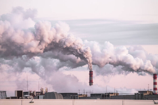 industrial chimneys with heavy smoke causing air pollution as ecological problem on the pink sunset sky background