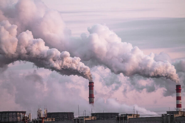 industrial chimneys with heavy smoke causing air pollution as ecological problem on the pink sunset sky background