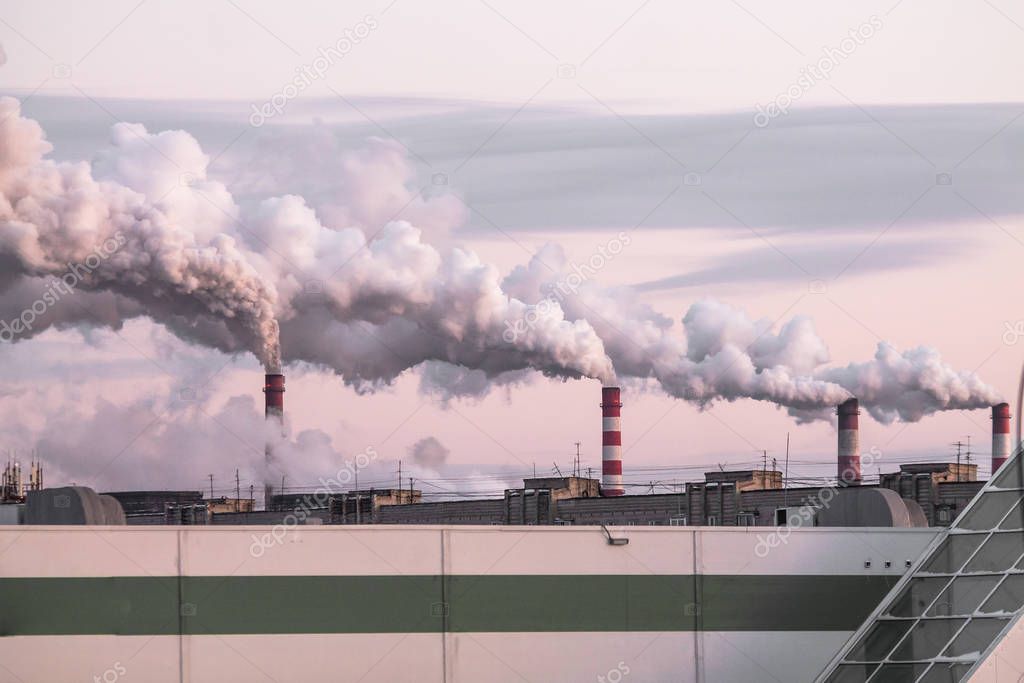 industrial chimneys with heavy smoke causing air pollution as ecological problem on the pink sunset sky background