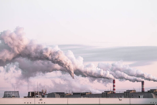 industrial chimneys with heavy smoke causing air pollution as ecological problem on the pink sunset sky background
