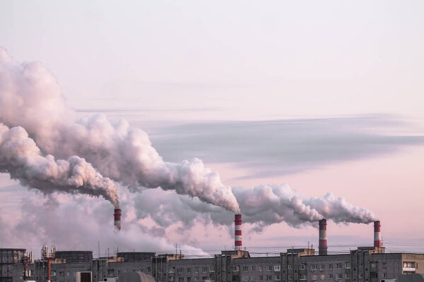 industrial chimneys with heavy smoke causing air pollution as ecological problem on the pink sunset sky background