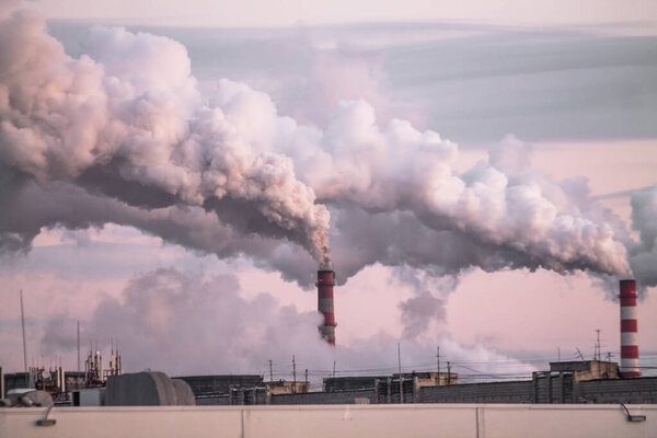 industrial chimneys with heavy smoke causing air pollution as ecological problem on the pink sunset sky background