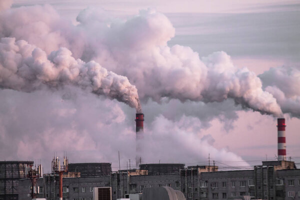 industrial chimneys with heavy smoke causing air pollution as ecological problem on the pink sunset sky background
