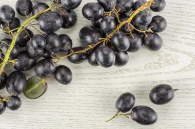 Black grape cluster (autumn royal variety) with three berries table top isolated on grey wood backgroun clipart