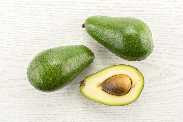 Two green smooth avocado and one section half with a seed table top isolated on grey wood background bacon variet