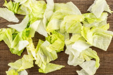 Iceberg lettuce fresh torn salad leaves table top isolated on brown wood backgroun clipart
