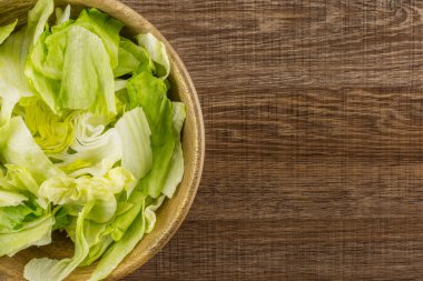 Göbek salatayı taze yırtık salata üzerinde kahverengi ahşap adam izole bir ahşap kase masa üstü bırakır