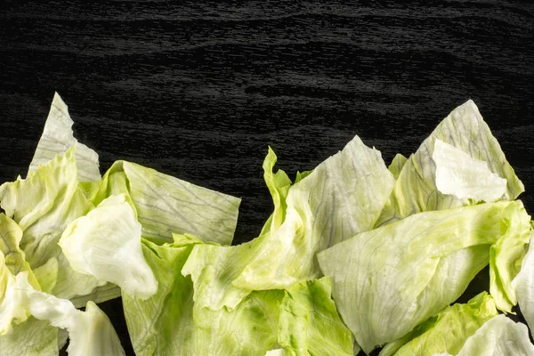 Iceberg lettuce fresh torn salad leaves stack table top isolated on black wooden backgroun