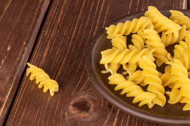Kahverengi ahşap üzerinde seramik bardak altlığı olan sarı fusilli makarna.