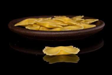 Bir sürü sarı makarna farfalle. Önünde kahverengi seramik bardak altlığı, siyah camda izole edilmiş.