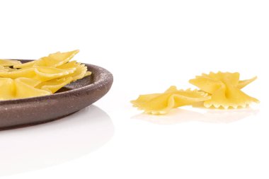 Beyaz arka planda izole edilmiş kahverengi seramik bardak altlığı olan bir sürü sarı makarna farfalle.