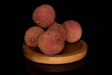 Siyah camla izole edilmiş bambu altlığı üzerinde beş taze lychee yığını.