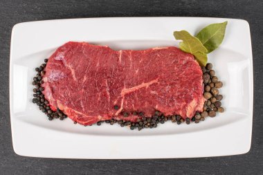 Güzel çiğ sığır filetosu, beyaz dikdörtgen seramik tabakta gri taşın üzerinde baharatlar.