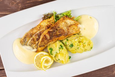 Kırık patatesli zander beyaz dikdörtgen seramik tabakta kahverengi ahşap üzerinde düz tabaka