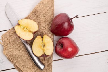 İki koca parça kırmızı elmadan oluşan bir grup jüt kumaş üzerinde lezzetli bir elma ve beyaz ahşap üzerinde de Santoku bıçağı.