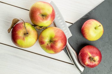 Gri taşın üzerinde taze bir bahçe elması ve beyaz ahşap üzerinde Santoku bıçağı olan beş kişilik bir grup.