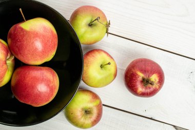 Bir sürü taze bahçe elması, siyah kasede, beyaz tahtada.