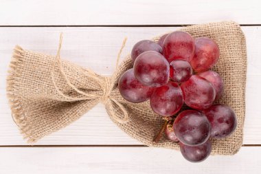 Bir sürü taze kırmızı dünya üzümü jüt çantasının üzerinde beyaz ahşap jüt torbasıyla.