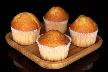 Dört küçük kekten oluşan bir grup, ahşap kare tabakta, siyah camla izole edilmiş.