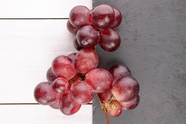 Lot of whole fresh red globe grape on stone and on white wood