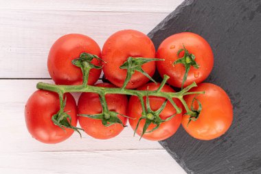 Bir sürü taze kırmızı kiraz domatesi ve beyaz ahşap üzerinde gri bir taş.