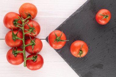 Bir sürü taze kırmızı kiraz domatesi beyaz ahşap üzerinde gri taş