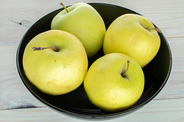 Group of four whole green delicious apple in bowl on white wood