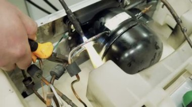 Servis Merkezi. Elektronik Onarım. Bir adam buzdolabı onarır. Alüminyum lehimleme.