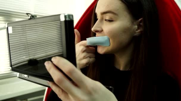 Jeune cliente assise dans une chaise rouge brosse les dents à l'aide d'un tissu en nylon habillé sur son index pour nettoyer en profondeur les dents — Video