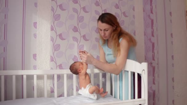 A mother putting her cute and happy newborn baby boy in a crib for his. — Stock Video