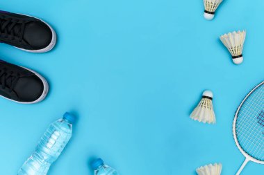 Spor malzemelerinin en iyi görüntüsü. Siyah spor ayakkabılar, su, Shuttlecock ve badminton raketi mavi arka plan ve arka planda. Spor hayatı kavramı.
