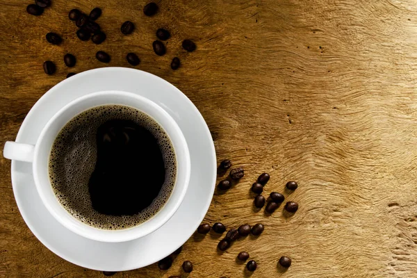 Von oben, schwarzer Kaffee mit Kaffeebohnen auf Holztischhintergrund. Konzept Kaffee trinken und entspannen — Stockfoto