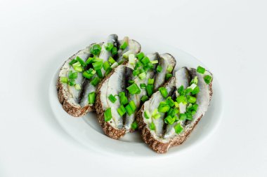 Üç lezzetli sandviç, çavdar ekmeği, tereyağı, küçük sardalyalar ve beyaz bir tabakta yeşil soğan.
