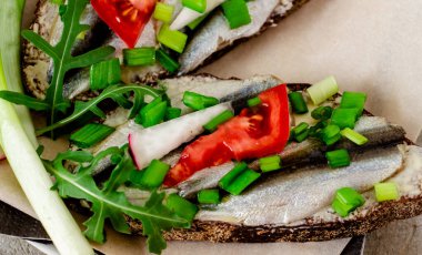 Çavdar ekmekli, tereyağlı, küçük sardalyeli, domates dilimli, turplu ve yeşil soğanlı lezzetli sandviçler. Beton parşömen üzerinde, sıra dışı bir yemek sunumu.