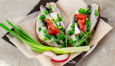Çavdar ekmekli, tereyağlı, küçük sardalyeli, domates dilimli, turplu ve yeşil soğanlı lezzetli sandviçler. Beton parşömen üzerinde, sıra dışı bir yemek sunumu.