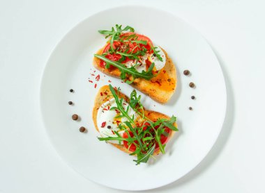 Lezzetli haşlanmış yumurta, beyaz bir tabakta domates, roka, baharat ve karabiber dilimli buğday dilimli ekmek.