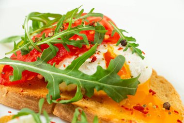 Lezzetli haşlanmış yumurta, beyaz bir tabakta domates, roka, baharat ve karabiber dilimli buğday dilimli ekmek.