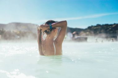 rear view of young woman relaxing in hot pool in Iceland  clipart