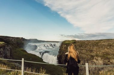 back view of young woman looking at scenic majestic waterfall in Iceland  clipart