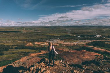 back view of young woman standing on cliff and looking at majestic landscape in Iceland clipart