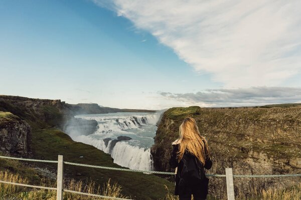 back view of young woman looking at scenic majestic waterfall in Iceland 