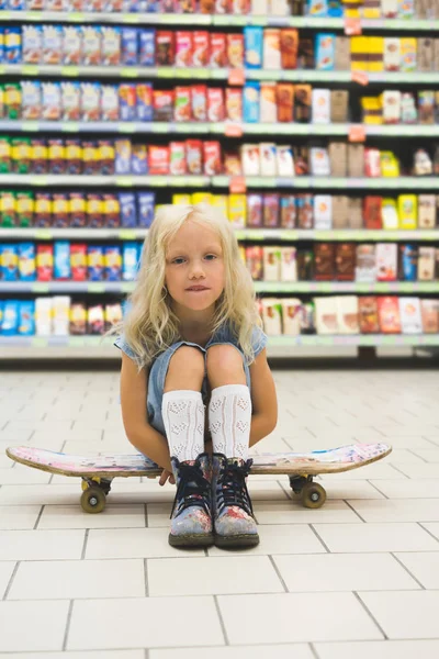 Adorable Blonde Child Sitting Skateboard Supermarket Shelves — Free Stock Photo