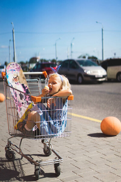 little female child eating chips while sitting in shopping cart with skateboard