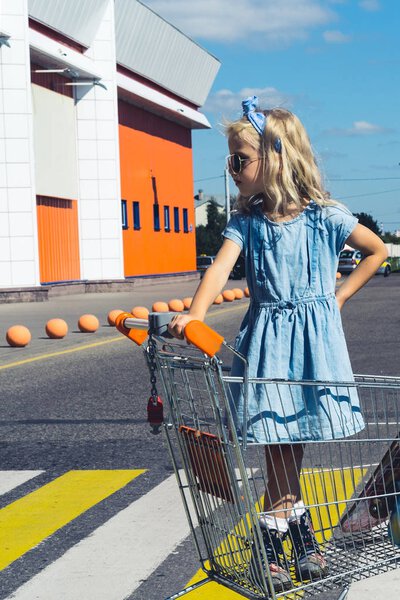 stylish kid having fun in shopping cart at parking
