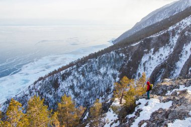 view of mountain slope with snow and trees and standing man,russia, lake baikal  clipart